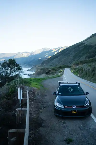 A black Volkswagen GTI parked beside a winding coastal road